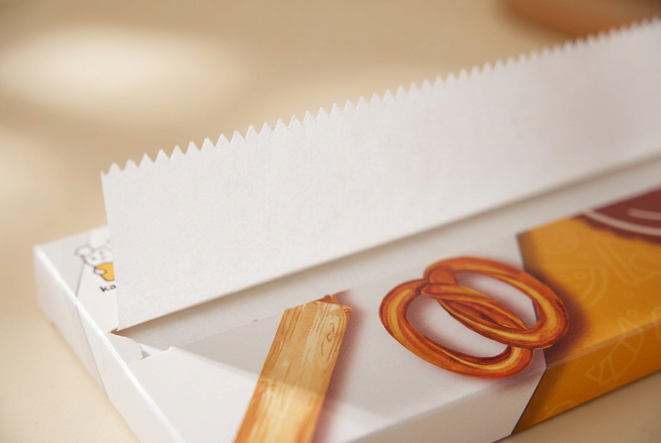 Pre-Cut Baking Paper Sheets with a serrated white edge standing in a printed pretzel themed box on a warm cream surface.